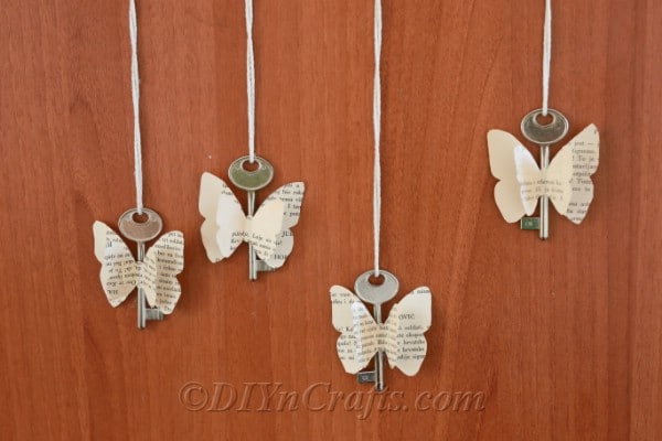 Rustic butterfly decorations made from old book pages and keys are displayed against a wood backdrop.