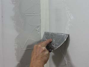 photo smoothing a first coat of joint compound on an inside drywall corner