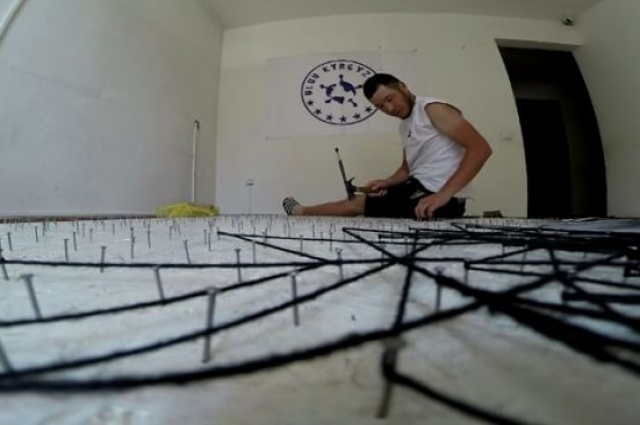 Азамат забивает в панно гвозди, а потом натягивает на них нитки.