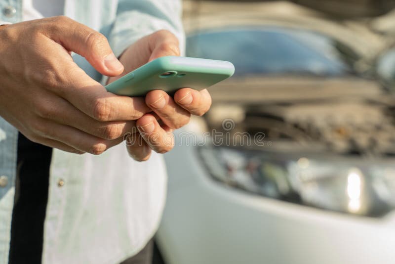 Close up hand of woman using smartphone and blur of her broken car parking on the road. Contacting car technician or royalty free stock photography