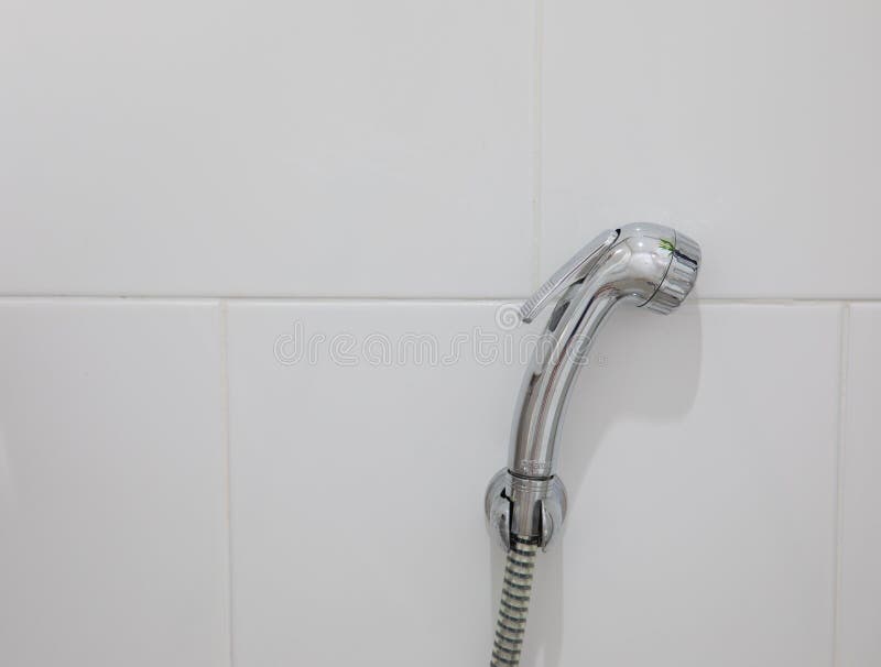 Shinny toilet shower hanging on white tiles wall. Front view and closeup photo of the toilet shower made of steel with shinny surface and hanging on the wall of stock photo