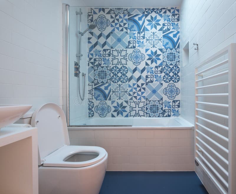 Modern bathroom with bath, toilet, niche in wall and basin unit, blue rubber floor and blue and white patchwork tiles. Above the bath royalty free stock photos