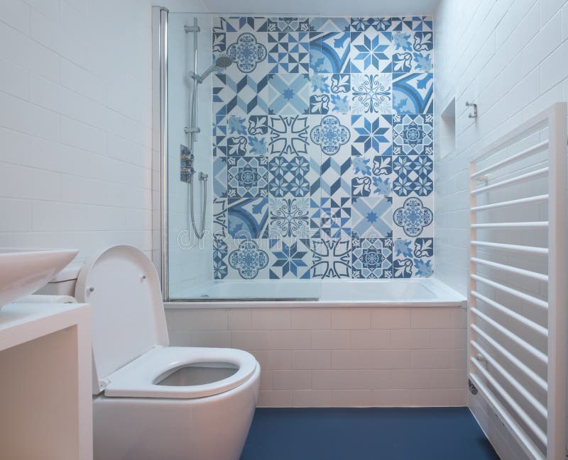 Modern bathroom with bath, toilet, niche in wall and basin unit, blue rubber floor and blue and white patchwork tiles. Above the bath stock image