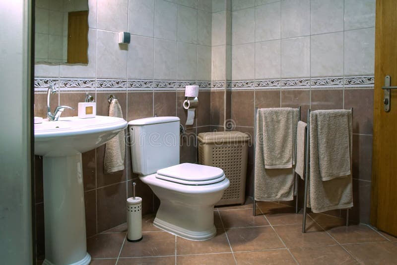 Modern brown bathroom with sink, toilet bowl, towels and brown tiles. Modern brown bathroom with sink, toilet bowl, towels and white and brown tiles stock photos