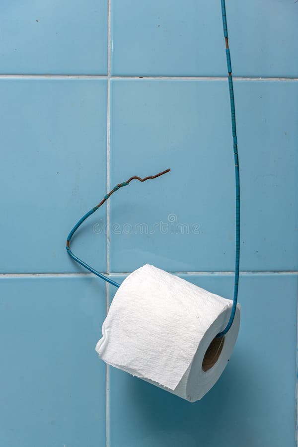 A roll of toilet paper hangs on a wire on a wall from blue tiles. Simple toilet paper holder at bathroom stock photos