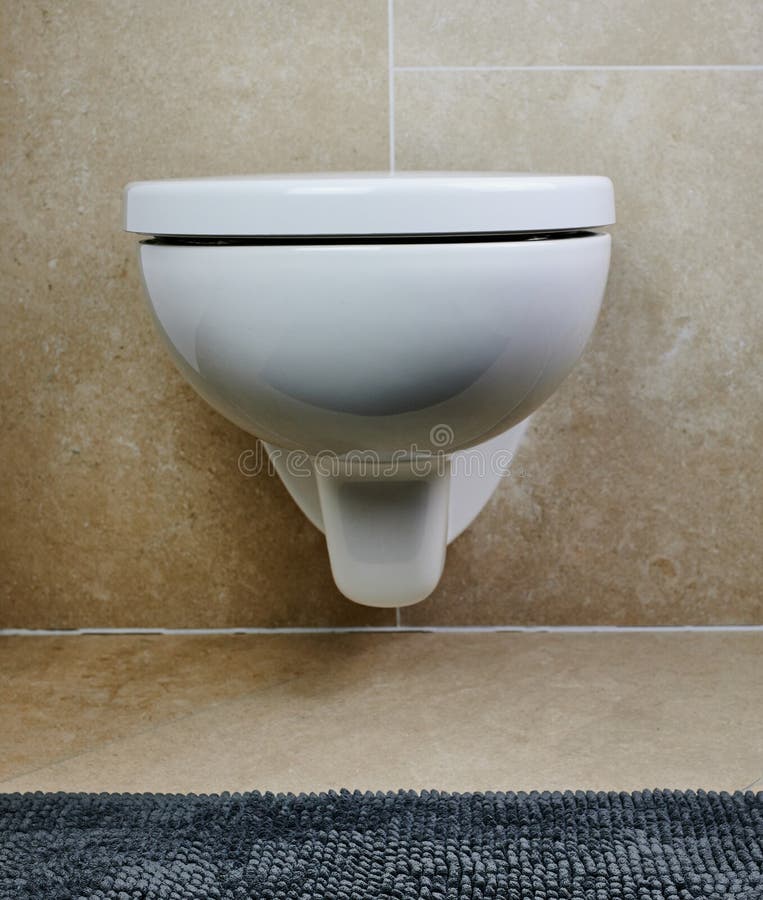 Wall-mounted toilet in white color against brown bathroom tiles. Wall-mounted white toilet against brown tiles in a private bathroom stock image
